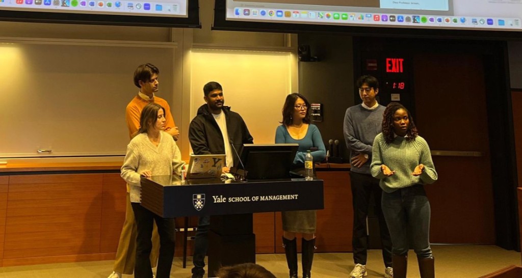 Vik Guttikonda at the Yale School of Management podium with a multinational cohort presenting a Business & Society capstone